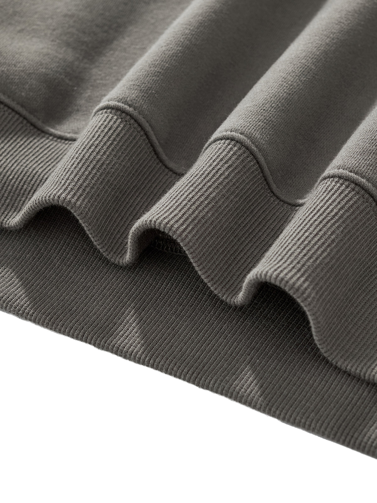 Detail of the fabric folds and ribbed hem of a unisex boxy hoodie in a muted color.